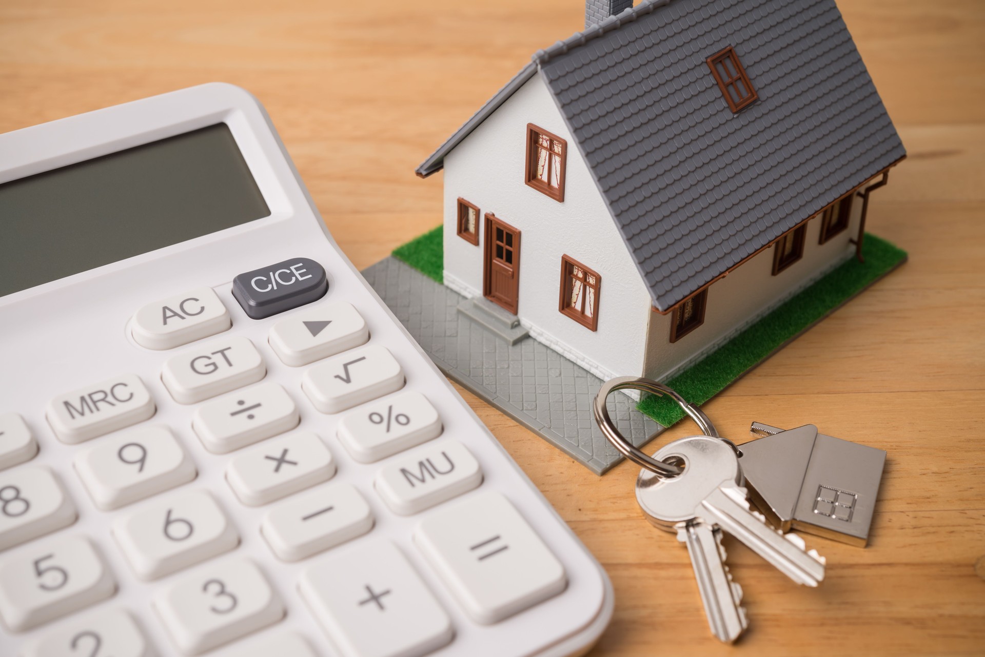 House model, key and white calculator on wooden table background.